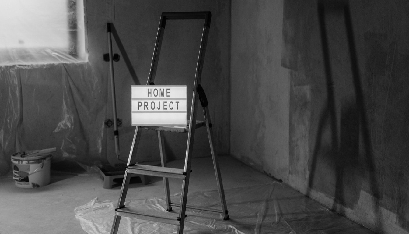 Stepladder holding a lit Home Project sign in a room prepared for renovation, with plastic sheeting over the floor and window
