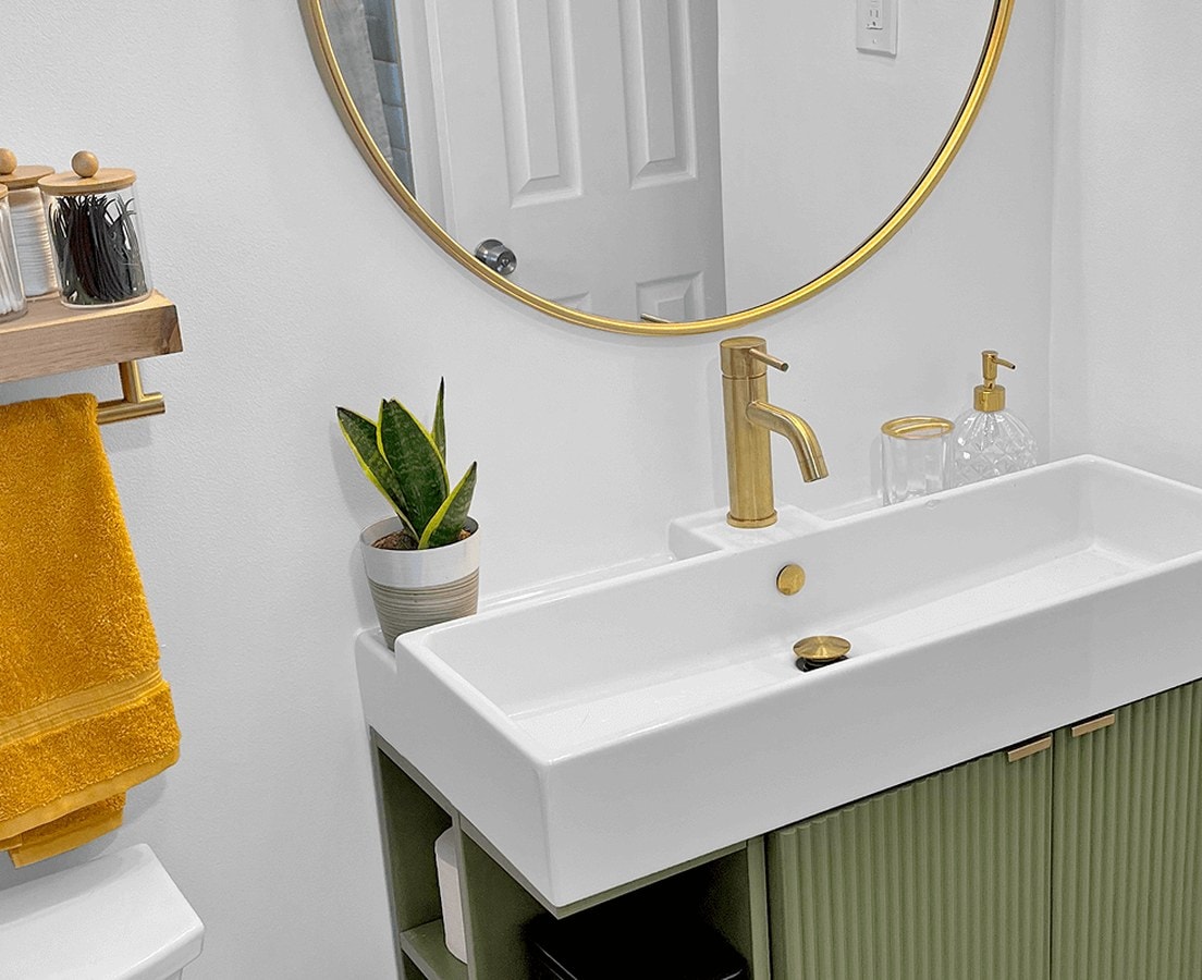 Guest bath with a trough sink on a green fluted vanity, brass faucet, and round brass mirror