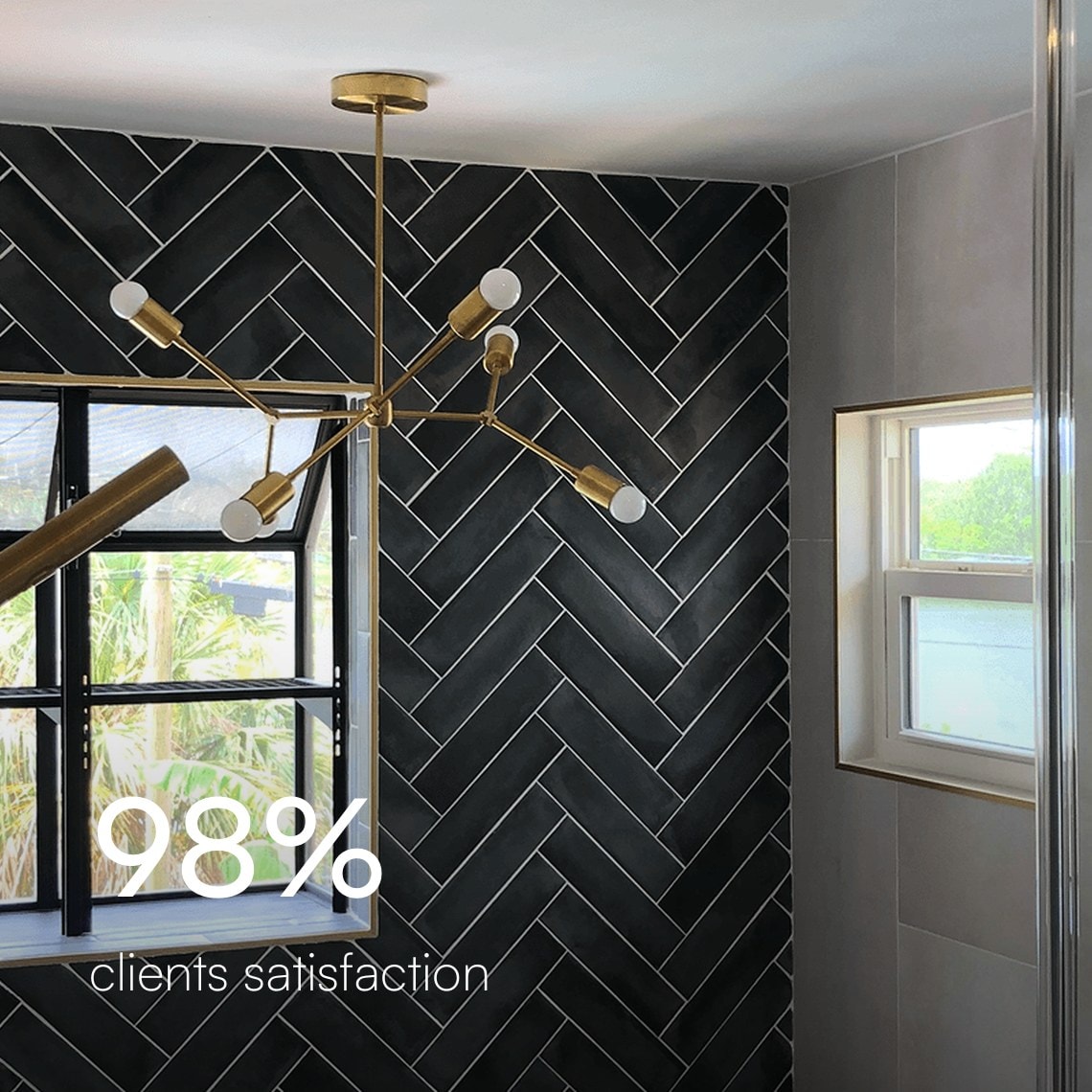 Charcoal herringbone tile wall with a window and a brass light fixture in an Ethicore bathroom, 98% client satisfaction