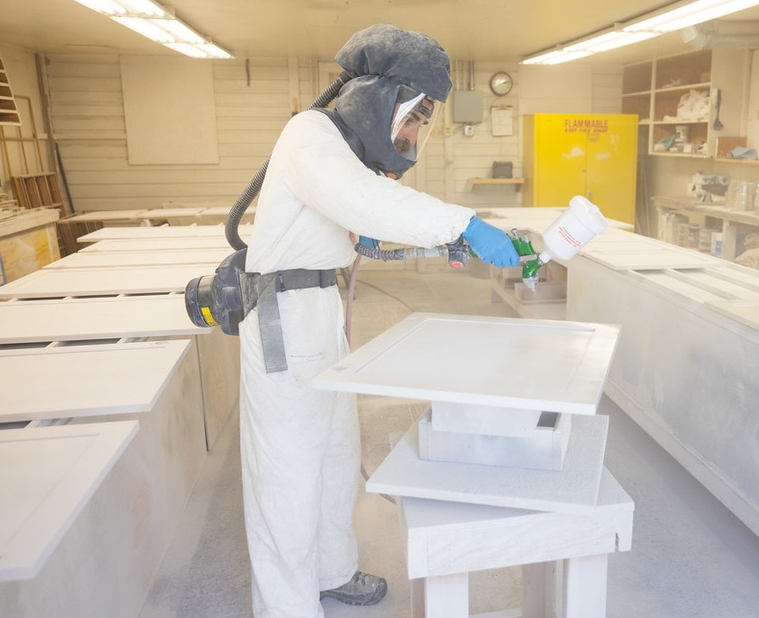 Finisher in a respirator spray-painting shaker cabinet doors in a spray booth