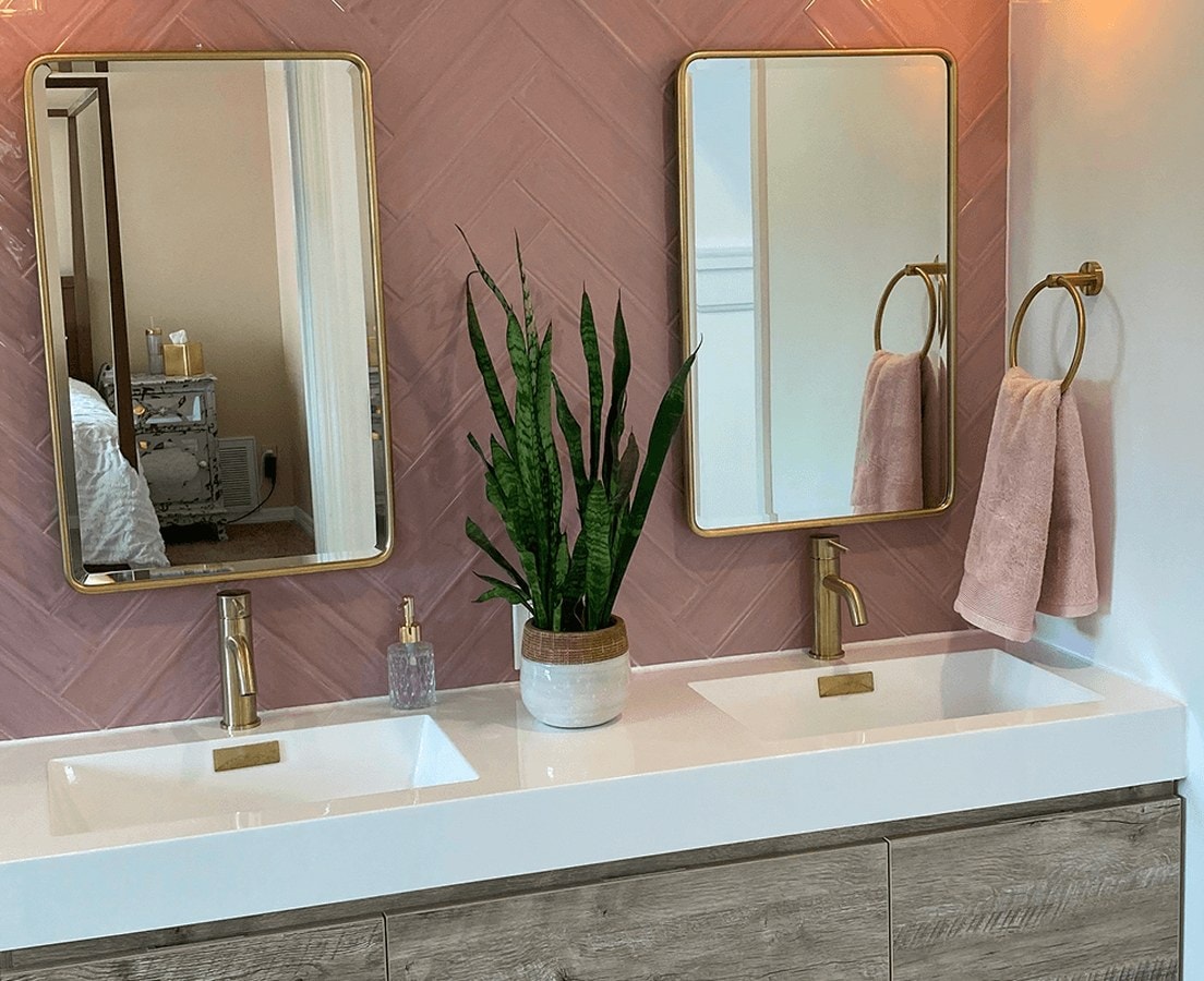 Floating wood-grain vanity with double sinks below brass mirrors