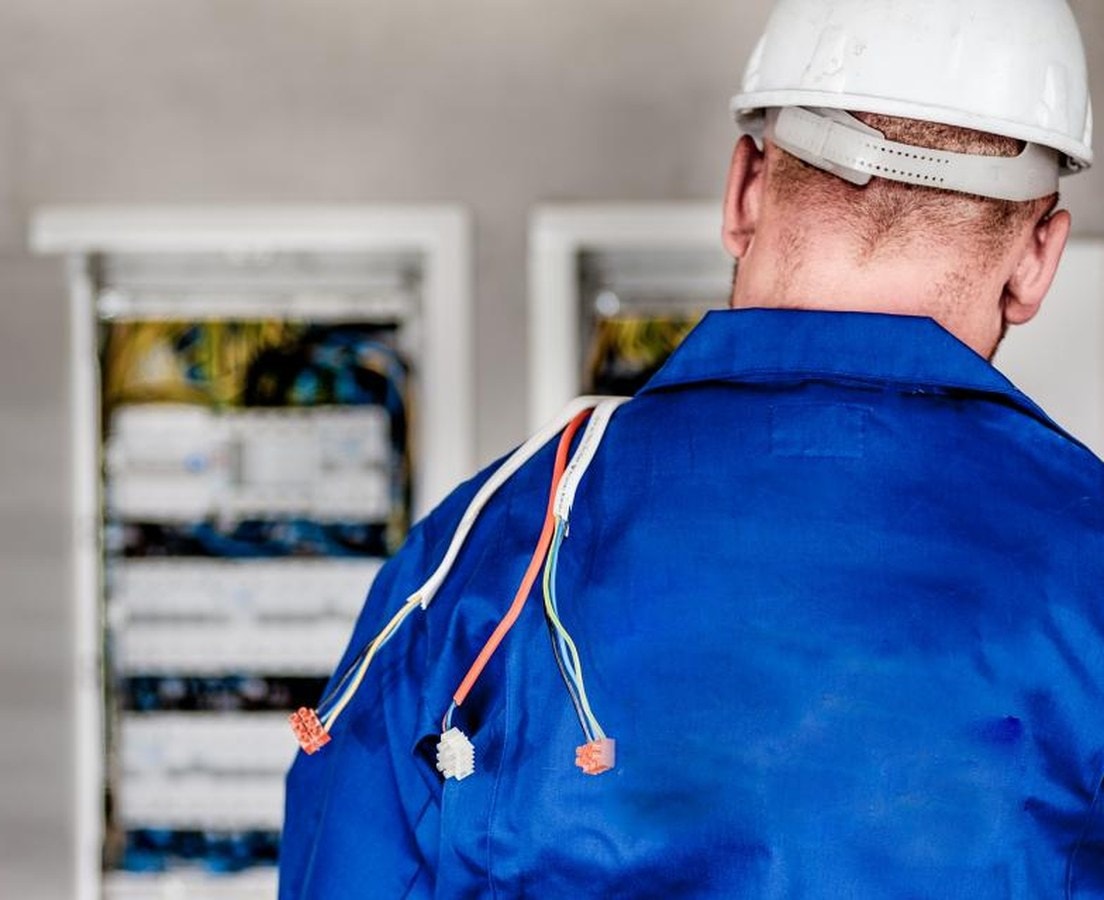 Electrician in a hard hat looking over an open breaker panel