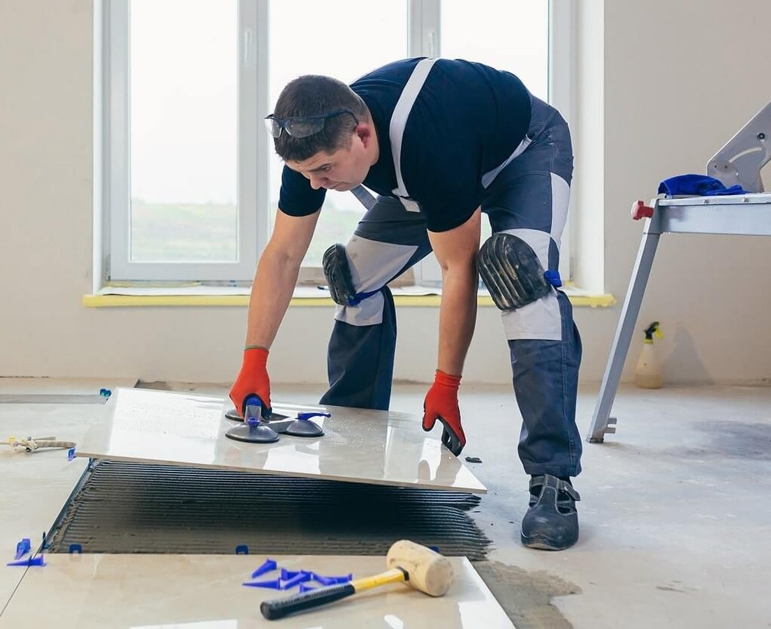 Installer lowering a large-format porcelain tile onto combed thinset with suction cups