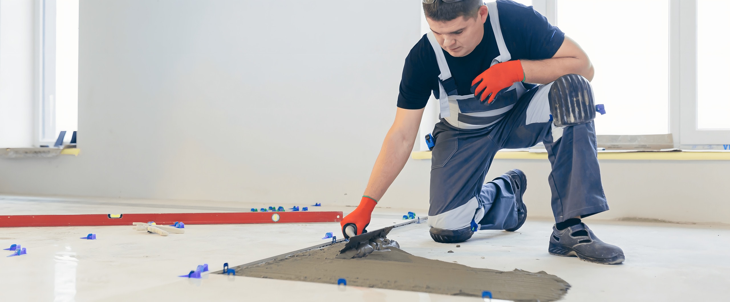 Tile setter combing thinset with a notched trowel between leveling clips on a porcelain tile floor