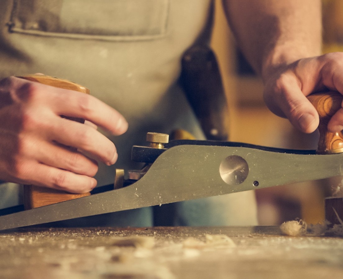 Carpenter trimming a piece of wood with a hand plane at the bench