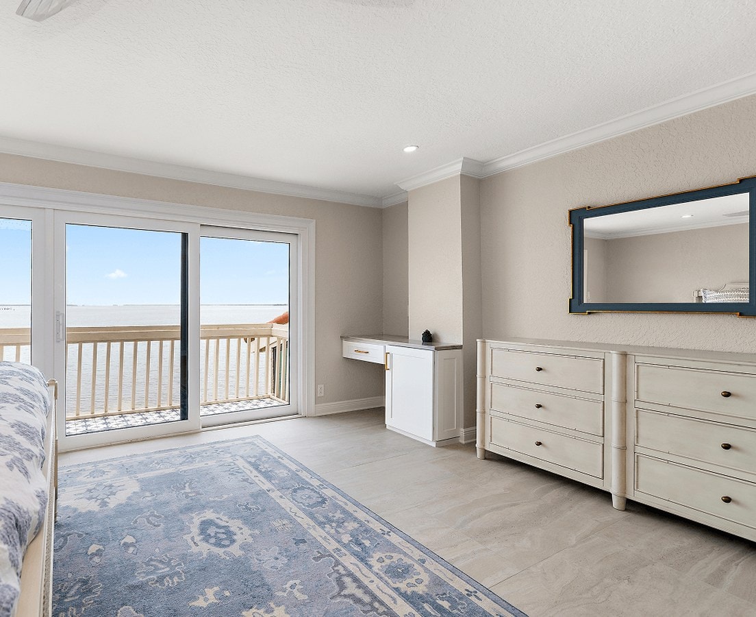 Bedroom with crown molding, a white dresser, and sliding doors to a balcony over the water