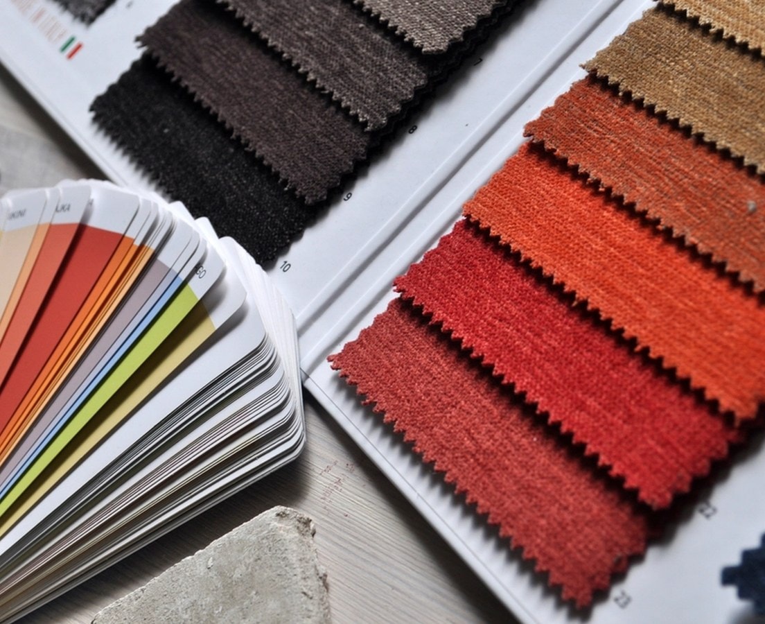 Paint color fan laid beside upholstery fabric swatches in brown, rust, and red