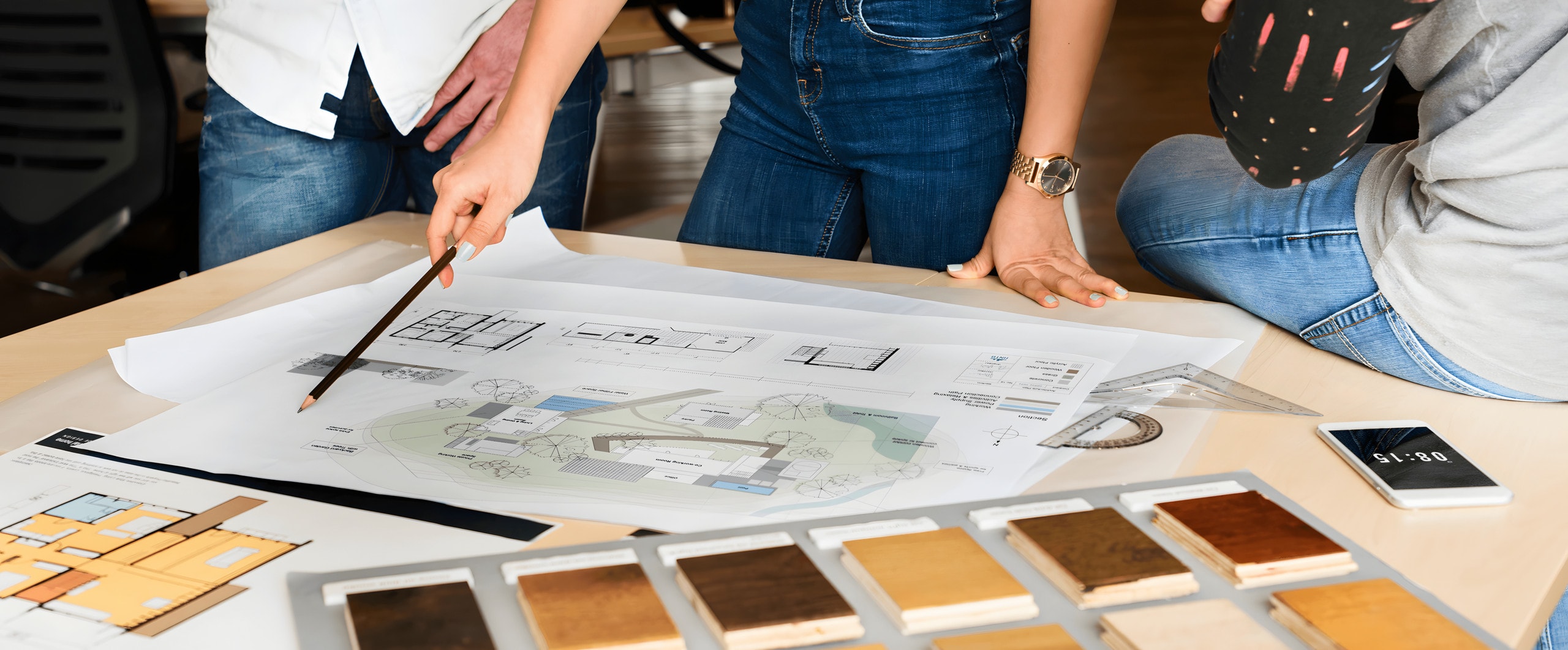 Designers reviewing a site plan and floor plans beside a tray of wood flooring samples