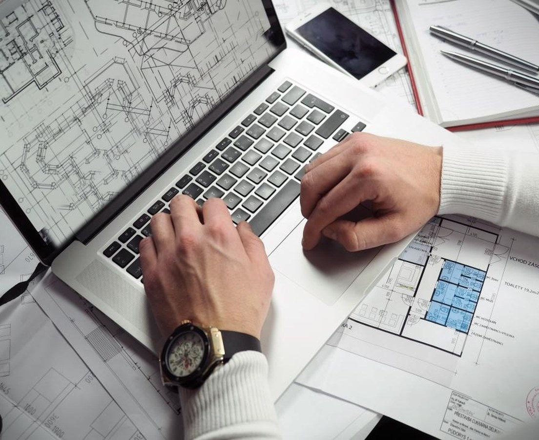 Designer working on floor plans on a laptop beside printed layout drawings