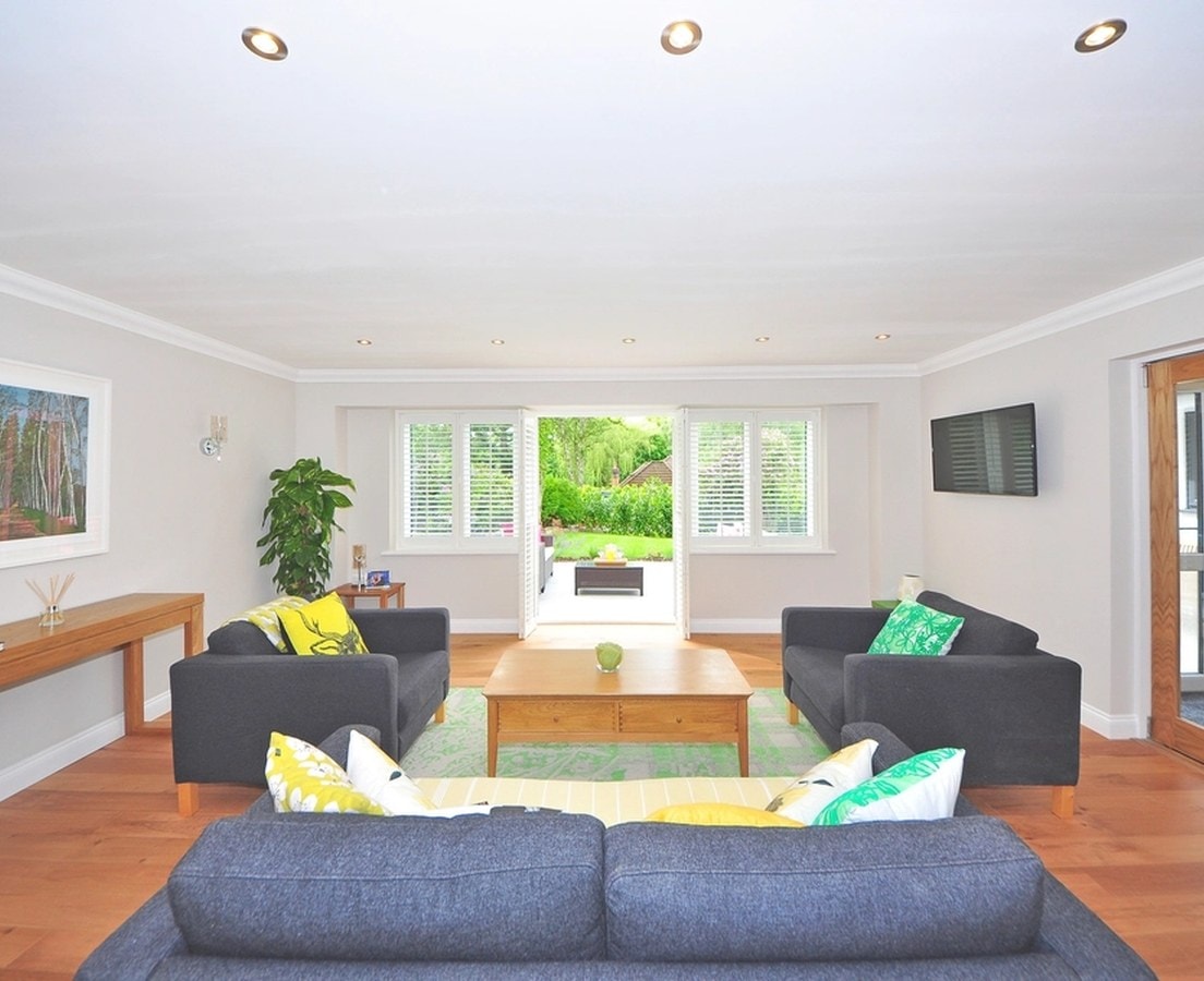 Styled living room with charcoal sofas, bright cushions, and doors open to the garden