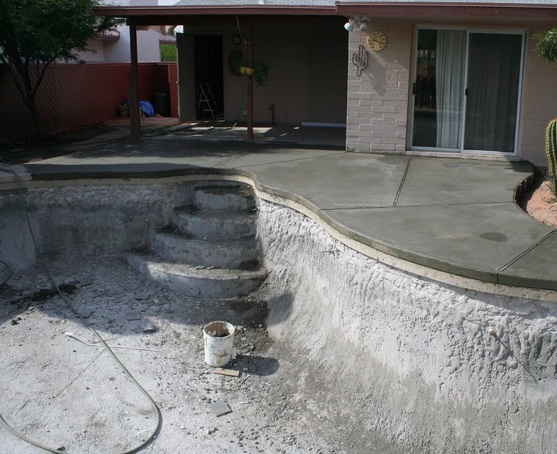 Freshly poured concrete deck around a stripped backyard pool during a remodel