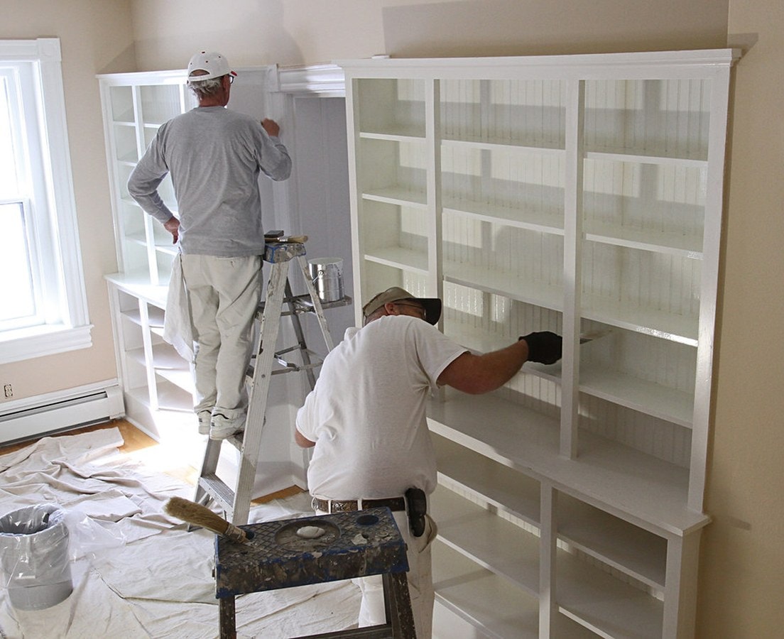 Two painters on a drop cloth painting white built-in bookshelves