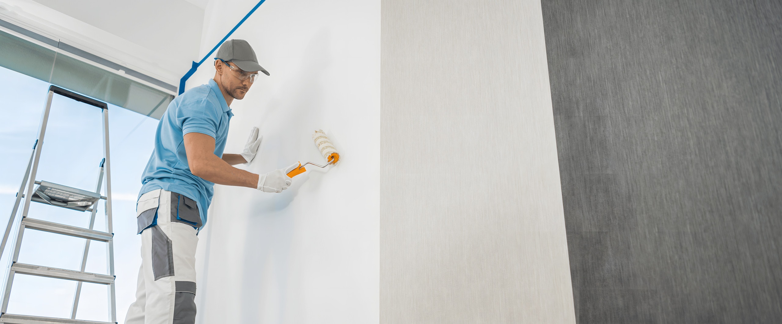 Painter rolling white paint onto a wall, shown beside light gray and charcoal textured wallcovering