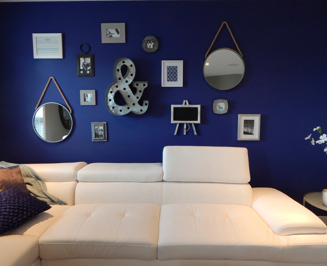 Navy blue accent wall with mirrors and framed prints above a white sectional sofa