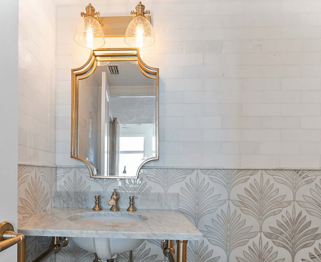 Finished powder room with a brass mirror, marble console sink, and patterned tile