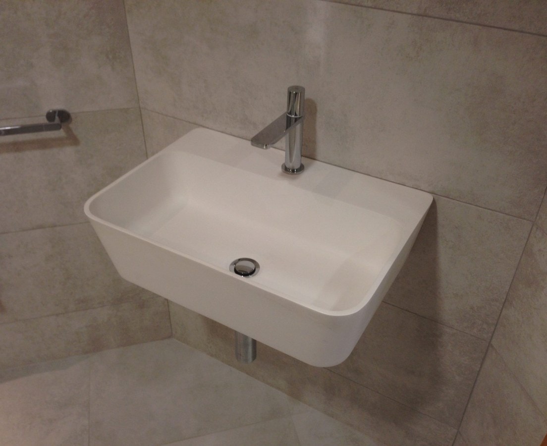 Wall-hung white sink with a single-lever chrome faucet on large stone-look tile