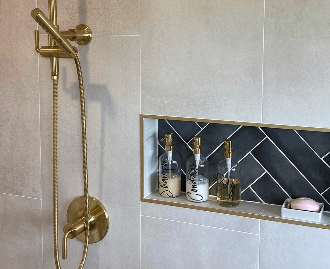 Brushed brass shower column with a handheld shower, valve trim, and a tiled niche