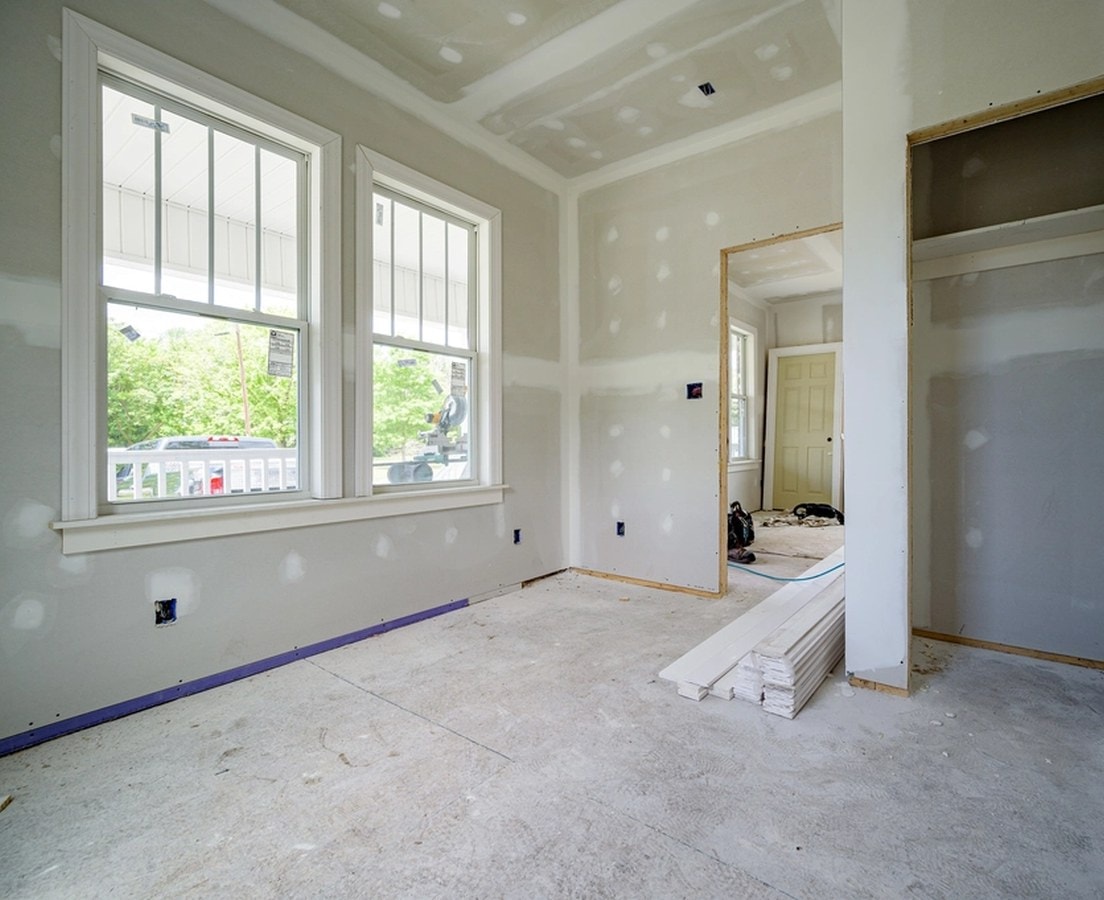 Drywalled rooms with new double-hung windows and a stack of trim boards, partway through a renovation