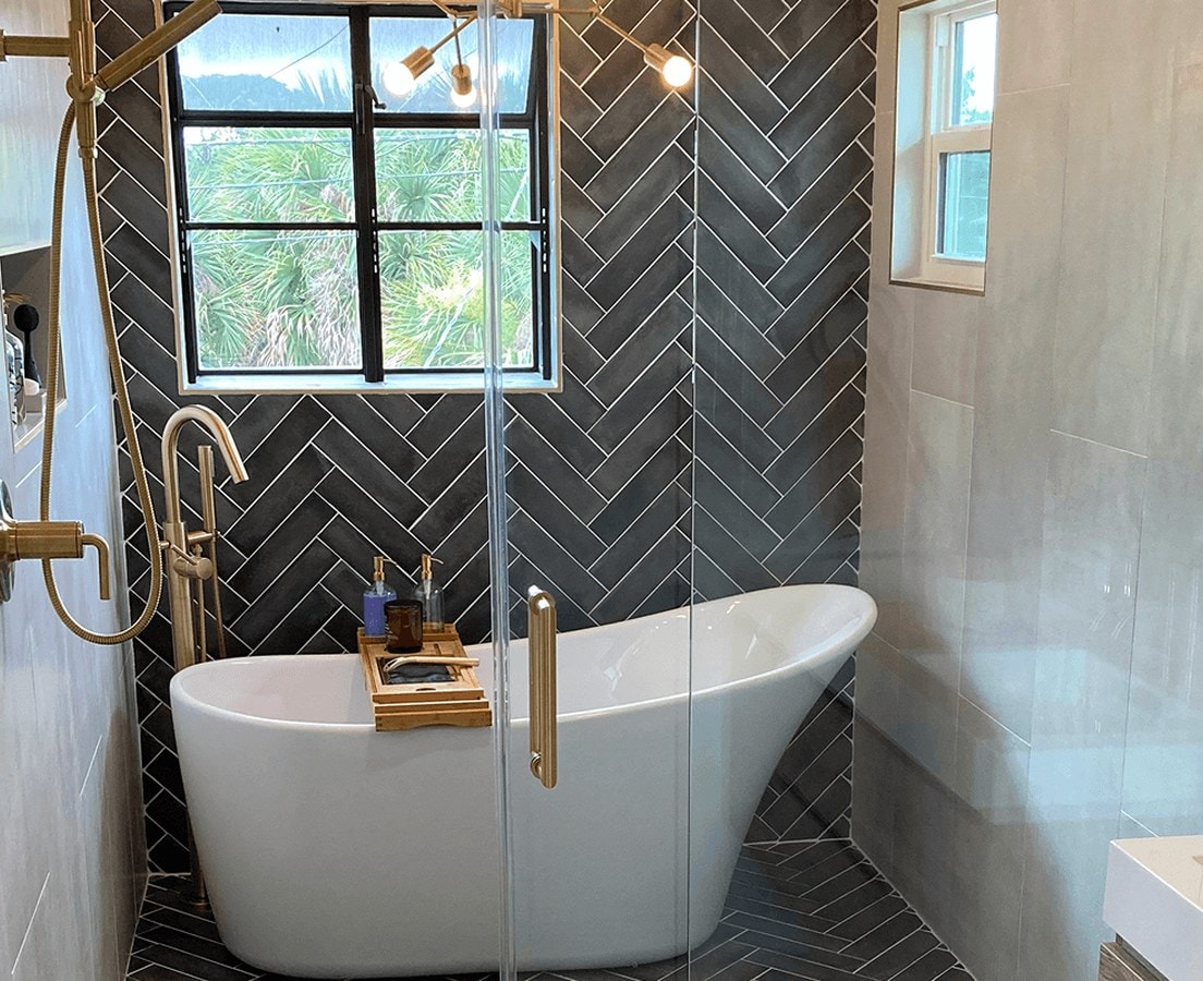 Finished bathroom with a freestanding tub, black herringbone tile, and brass fixtures